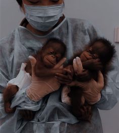 a woman wearing a surgical mask holding three baby oranguels in her arms