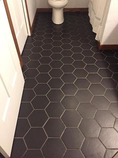 a white toilet sitting in a bathroom next to a sink and shower stall with black tile on the floor