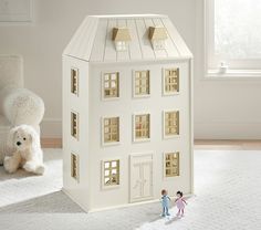 two small dolls are standing in front of a doll house with a teddy bear on the floor