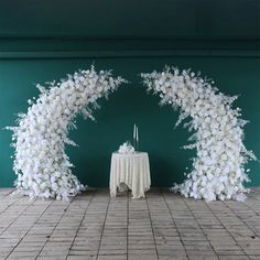 an arch made out of white flowers on top of a brick floor next to a table