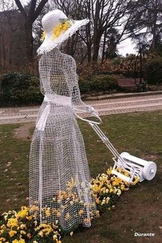 a woman with a lawn mower and flowers in front of her, on the grass