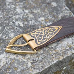 a gold and brown leather keychain with an intricate design on the front, sitting on a rock