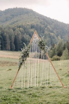 a wedding arch decorated with flowers and greenery in front of a green mountain range