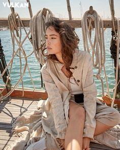 a woman sitting on top of a boat next to the ocean with ropes hanging from it