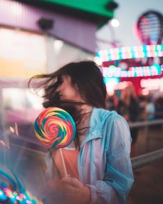 a woman holding a lollipop in front of a carnival