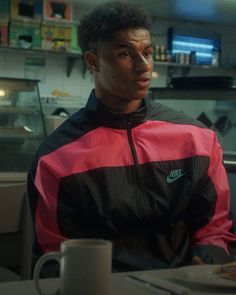 a man sitting at a table with a plate of food in front of him and looking off into the distance