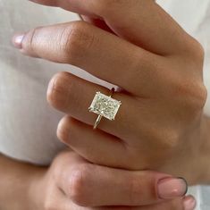 a woman's hand holding a ring with a square shaped diamond in the middle