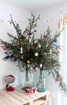 a christmas tree sitting on top of a wooden table next to two vases filled with ornaments