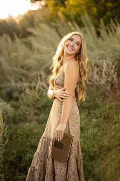 a beautiful young woman in a long dress holding a brown purse and smiling at the camera