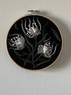 a black and white embroidered flower on a wall hanging from a metal frame with silver thread