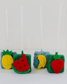 three candles with fruit designs on them sitting in front of a white wall and one candle is lit