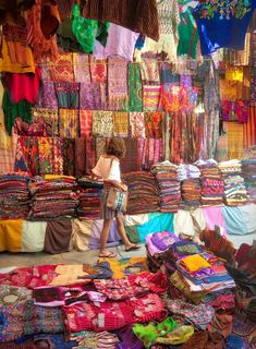 a woman walking through a market filled with lots of colorful items