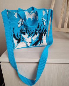 a crocheted blue purse sitting on top of a white dresser next to a wooden chair