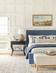 a bedroom with white walls, blue bedding and a large painting on the wall