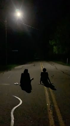 two people sitting on the side of a road at night