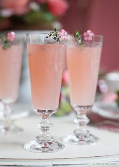 three wine glasses filled with pink liquid and garnished with flowers on the rim