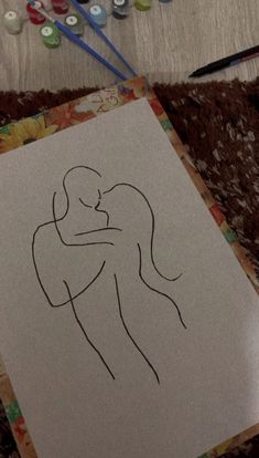 a drawing of two people hugging each other on a piece of paper next to markers and pens