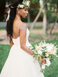 a woman in a wedding dress holding a bouquet and looking off into the distance with her back to the camera