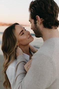 a man and woman standing next to each other near the ocean at sunset or sunrise