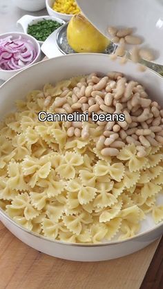 pasta and beans in a white bowl on a wooden table next to bowls of vegetables