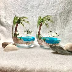 two wine glasses with palm trees painted on them and seashells in the foreground