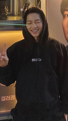 a man in a black hoodie is smiling and making the peace sign with his hand