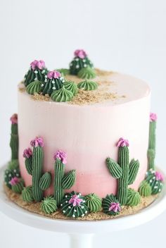 a cake decorated with pink frosting and green cactus decorations on a white platter