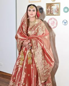 a woman in a red and gold bridal gown standing next to a wall with pictures on it