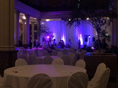 an indoor event with white linens and purple lighting