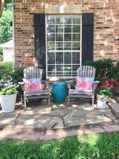 two chairs sitting in front of a window on top of a stone patio with potted plants