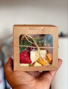 a hand holding up a box filled with different types of fruit