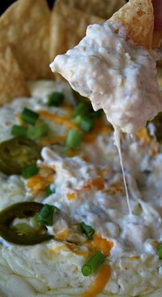 a tortilla chip being dipped with white cheddar cheese and green onions