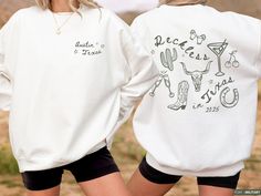 two women wearing white sweatshirts with cactus designs on the front and back, one in black shorts