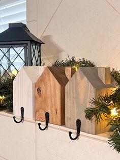 three wooden houses are mounted to the wall with hooks and lights on top of them