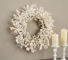 a white wreath and two candles on a table next to a wall mounted candle holder