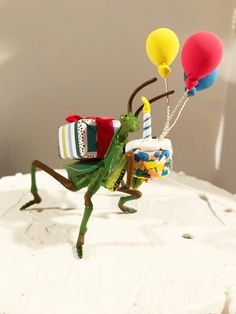 a cake topped with a green grasshopper holding balloons