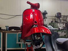 a red motor scooter in a garage next to a blue machine and some tools