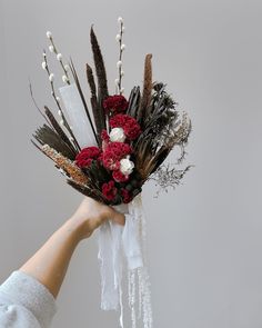 a person holding a bouquet of flowers in their hand with white and red flowers on it