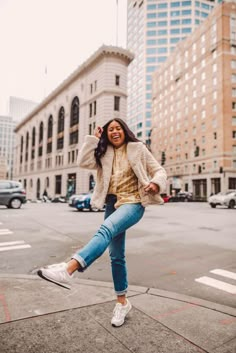 a woman is dancing on the sidewalk in front of some tall buildings and skyscrapers