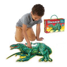 a young boy is playing with a toy dinosaur on the floor and in front of it's packaging