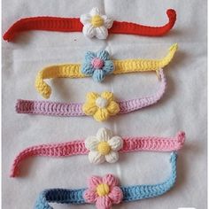 four crocheted headbands with flowers on them sitting on a white sheet