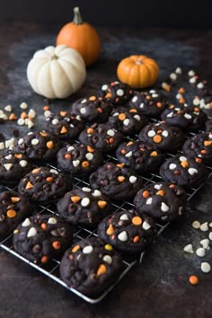 chocolate cookies with white and orange sprinkles on a cooling rack next to pumpkins