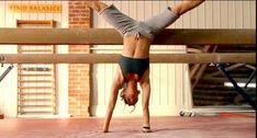 a woman doing a handstand on top of a wooden beam in a gym