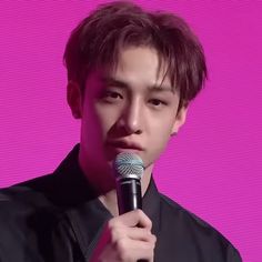 a young man holding a microphone in front of a purple background and wearing a black shirt