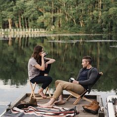 a man and woman sitting on chairs on a dock next to a body of water