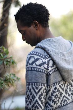 a man wearing a gray and black sweater with a white pattern on the back is looking down at his cell phone