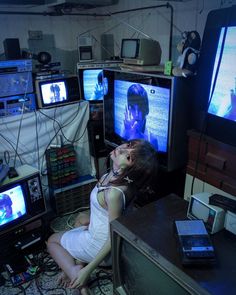 a woman sitting on the floor in front of televisions