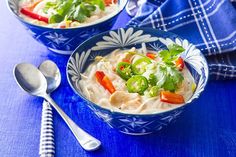 two bowls filled with soup on top of a blue table cloth next to spoons