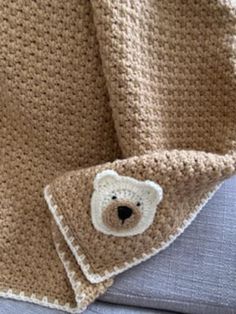 a crocheted blanket with a teddy bear on the front and back, sitting on top of a couch