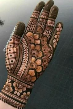 a hand that is decorated with henna and flowers on the palm, next to a body of water